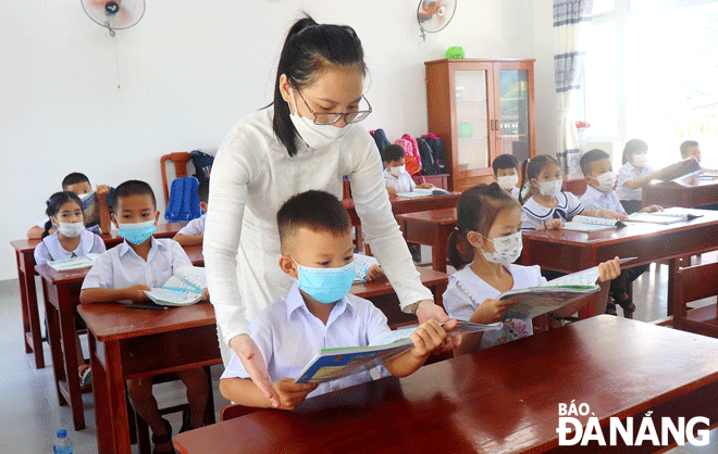 Học sinh lớp 1 điểm trường Phò Nam (xã Hòa Bắc) được giáo viên hướng dẫn cách cầm sách đúng tư thế trong ngày đầu đến trường. 		Ảnh: NGỌC HÀ