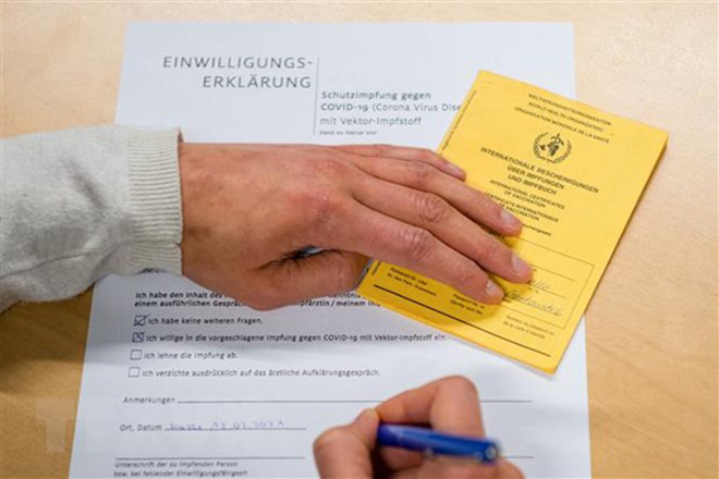 Người dân điền thông tin vào bản khai bên thẻ Chứng nhận tiêm vaccine ngừa Covid-19 do Tổ chức Y tế Thế giới (WHO) cấp phép, tại điểm tiêm chủng ở Halle/Saale, miền Đông Đức. (Ảnh minh họa: AFP/TTXVN)