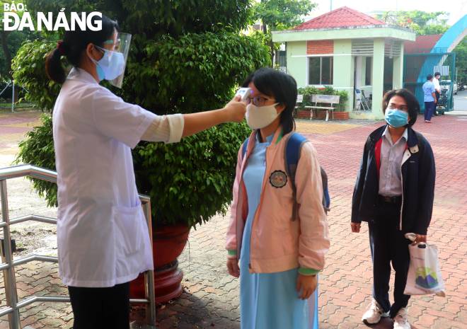 A school healthcare worker checks the temperature of 12th graders before entering the classroom.