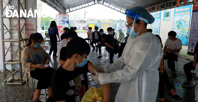 A health care professional is giving the Covid-19 vaccine to an eligible female student in mask