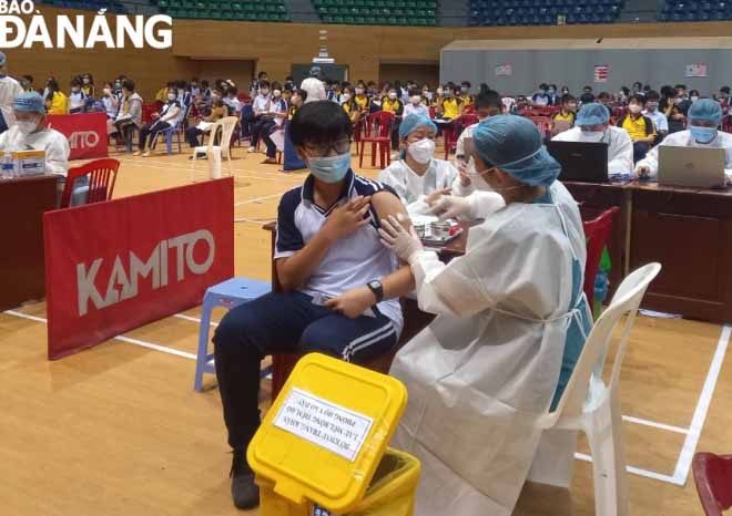 A healthcare professional wearing personal protective equipment giving a vaccine to an eligible male student in mask at the Tien Son Sports Arena. Photo: NGOC HA