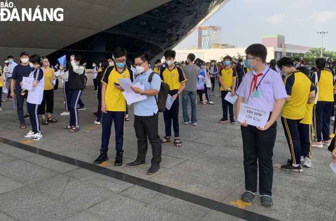 Students in grades 8 and 9 are guided by their teacher to prepare their COVID-19 vaccine documents while queuing outside the vaccination site at the Tien Son Sports Arena. Photo: NGOC HA