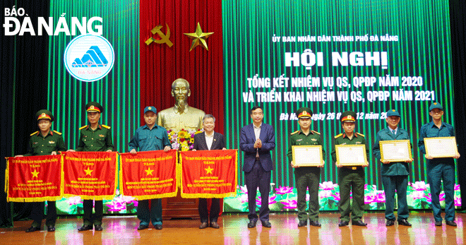 Chủ tịch UBND thành phố Lê Trung Chinh (giữa) tặng Cờ đơn vị dẫn đầu phong trào thi đua và bằng khen của UBND thành phố cho các tập thể hoàn thành xuất sắc nhiệm vụ quân sự, quốc phòng địa phương năm 2020. Trong đó, đại diện tập thể Phòng Chính trị (thứ tư, từ phải sang) nhận bằng khen.Ảnh: HỒNG HẠNH