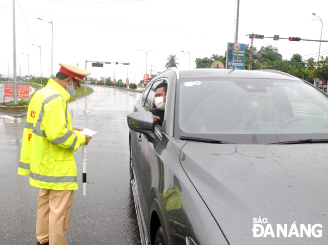 A traffic police officer pulling over a car driver to check his COVID-19 papers at a checkpoint on National Highway 14B in Hoa Nhon Commune, Hoa Vang District before he enters the city. Photo: LE HUNG