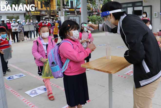 First graders of the Hai Chau District-based Ly Tu Trong Primary School have their body temperature checked before entering their classes.