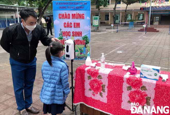 A teacher of the Ngo May Primary School instructing a first grader to measure her body temperature automatically.