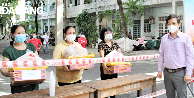 In light of complicated developments of COVID-19, authorities at all levels in Da Nang have been making efforts to ensure social welfare for local residents. IN THE PHOTO: Deputy Secretary of the Hai Chau District Party Committee Huynh Van Nhan (right cover) handing over essentials to people in a blockaded residential area in August 2021. Photo: LAM PHUONG