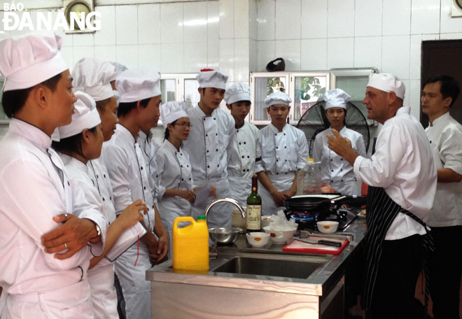 Sinh viên Trường Cao đẳng Nghề Việt - Úc (VAVC) đội mũ trắng thực hành nghề bếp với thầy giáo - chuyên gia ẩm thực nước ngoài (ảnh chụp lúc chưa xảy ra Covid-19). Ảnh: V.T.L