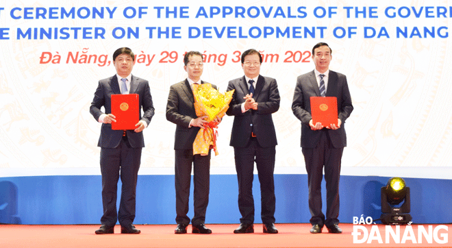 Deputy Prime Minister Trinh Dinh Dung (second from right) hands over decrees and decisions of the national government and the Prime Minister on the Da Nang development to Da Nang Party Committee Secretary Nguyen Van Quang (second, left); municipal Party Committee Standing Deputy Secretary cum municipal People's Council Chairman Luong Nguyen Minh Triet (left, first) and municipal Party Committee Deputy Secretary cum municipal People's Committee Chairman Le Trung Chinh, on March 29, 2021,  Photo: TRIEU TUNG