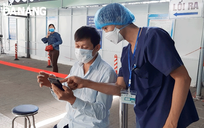 A healthcare worker at the Da Nang General Hospital helping an outpatient to fill in a COVD-19 declaration form online. Photo: PHAN CHUNG