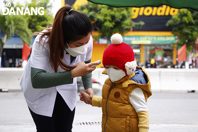 A teacher at the ABC Kindergarten checks the body temperature of a kid before taking her to the class. Photo: XUAN DUNG