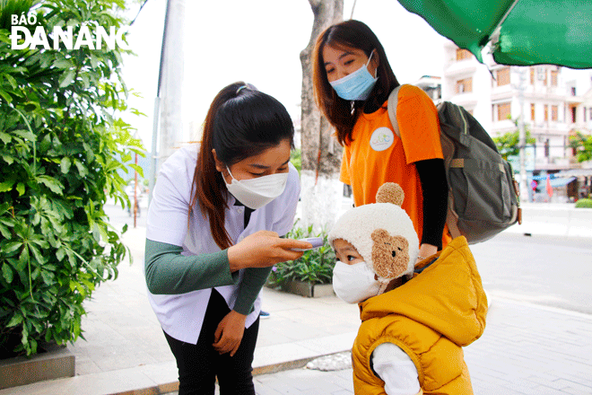 A local pre-school kid has her body temperature measured before entering class. Photo: Xuan Dung