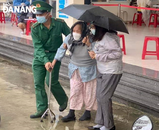 Chiên sĩ Biên phòng thành phố (trái) giúp người cao tuổi đi tiêm vắc-xin tại điểm tiêm thuộc Khu kí túc xá phía Tây thành phố.