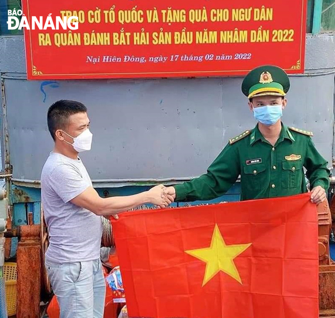 An officer from the Son Tra Border Guard Station (right) giving the national flag to a fisherman so as to encourage him to head out to sea in the protection of the homeland's sea and islands.