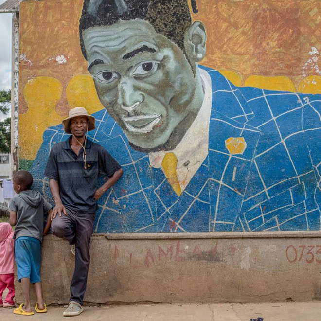 Nghệ sĩ đường phố Basil Matsika trước bức tranh tường của ông.  Ảnh: The Guardian