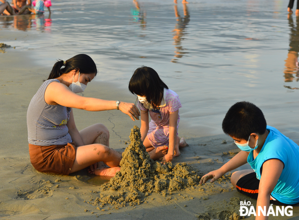 Children are seen playing sand castle building game with their family members. 