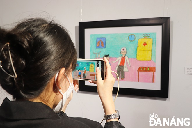 A young visitor taking souvenir photos of some paintings on display at the exhibition. Photo: Xuan Dung