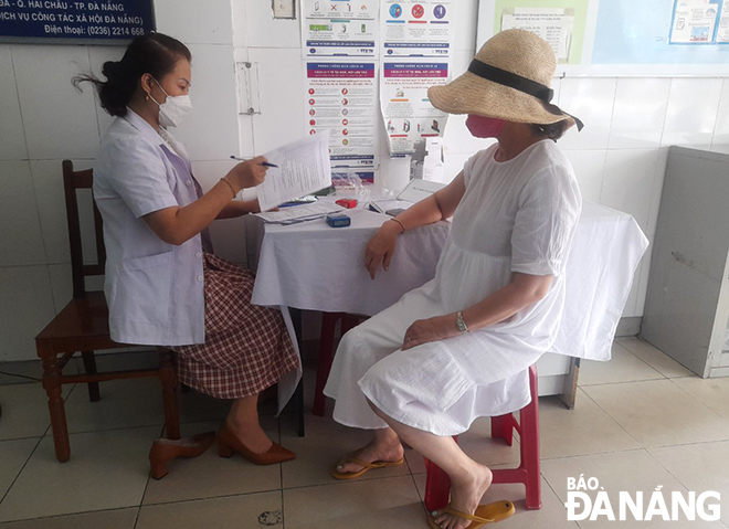 Cán bộ tại Trạm y tế phường Hải Châu 1 (quận Hải Châu) hướng dẫn người dân điền thông tin cá nhân trước tiêm.