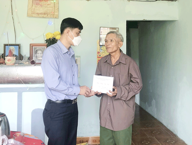 Mr. Thai Van Hoai Nam (left), the President of Hoa Bac Commune's People's Committee, gives gift to a war invalid who lives in poverty 