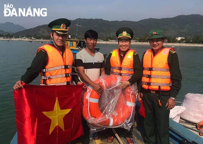 Thiếu tá Kiều Duy Tiến (thứ hai, phải sang) cùng đồng đội trao tặng cờ tổ quốc cho ngư dân ở quận Liên Chiểu. Ảnh: DOÃN QUANG