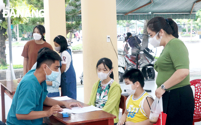 Phụ huynh đưa con đến tiêm vắc-xin tại điểm tiêm Trường THCS Nguyễn Huệ trong ngày 21-8. Ảnh: VĂN HOÀNG	
