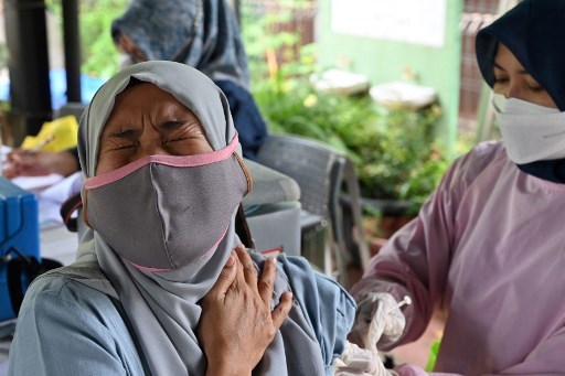 A woman (left) reacts while receiving a Pfizer booster vaccine for COVID-19 in Jakarta, on March 29. (Photo: AFP/VNA)