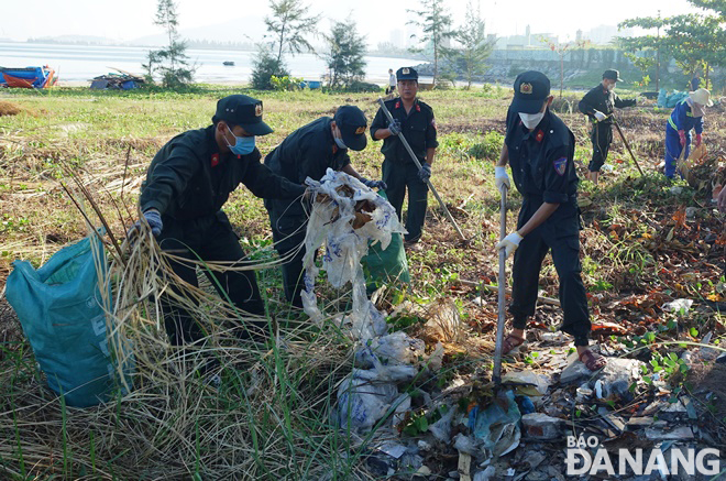 Mobile police officers are joining efforts with workers of the Da Nang Urban Environment Joint Stock Company to collect trash on a beach along Nguyen Tat Thanh Street. Photo: HOANG HIEP