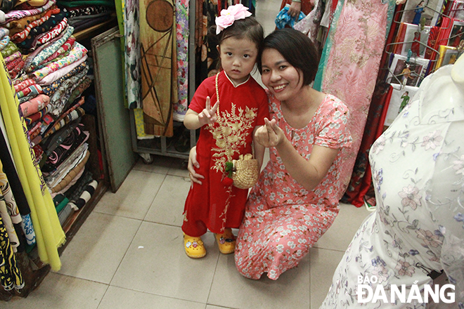 A South Korean baby girl in 'ao dai' taking a souvenir photo with a small trader in the Han Market