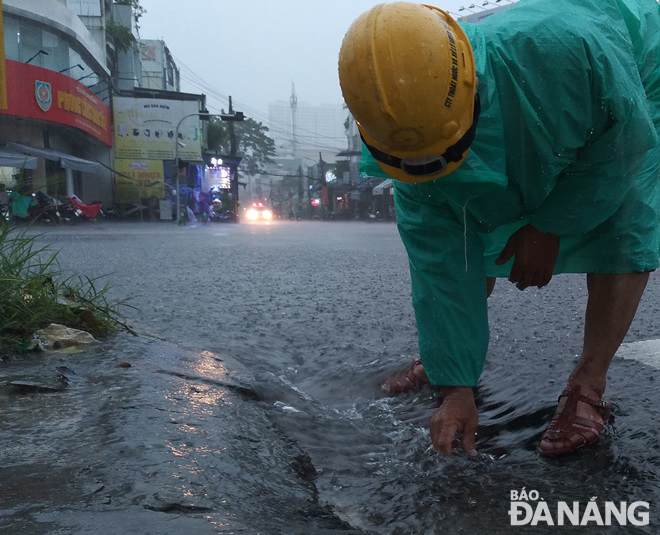 Một công nhân Công ty Thoát nước và xử lý nước thải Đà Nẵng thu gom rác ở các cửa thu trên mặt đường Lê Duẩn để nước nhanh thoát.