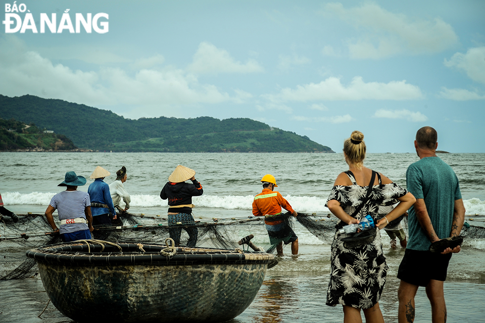 Foreign tourists witnessing fishermen pulling the fishing net on the beach.
