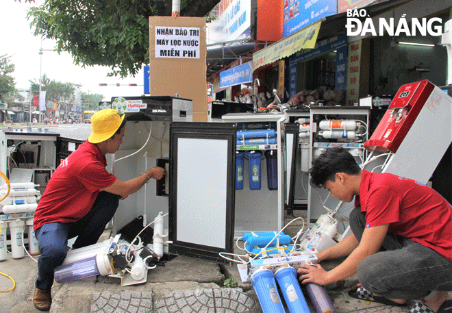 Anh Hồ Văn Đức, chủ cửa hàng máy lọc nước tại quận Liên Chiểu (bên trái) cùng thợ hỗ trợ sửa miễn phí máy lọc nước hư hỏng do ngập lụt. Ảnh: L.P	