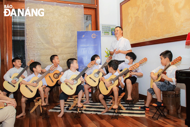 Nghệ sĩ guitar Phan Xuân Trí (hàng sau) hướng dẫn kỹ thuật chơi đàn cho các em thiếu nhi Đà Nẵng. Ảnh: X.D