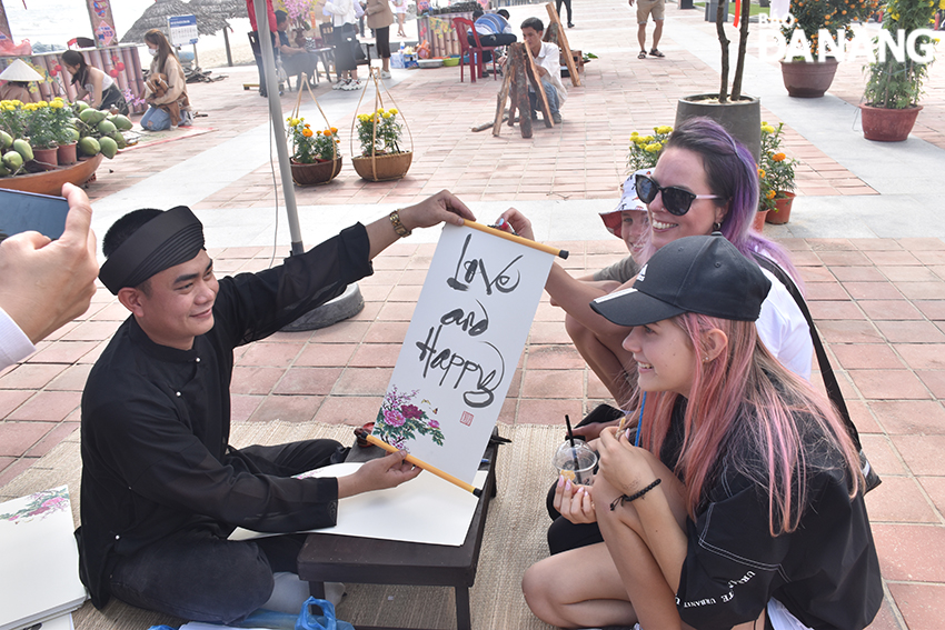 Visitors are delighted to receive calligraphy written in English. Photo: THU HA