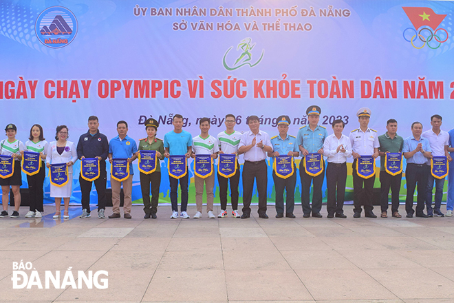 Giám đốc Sở Văn hóa và Thể thao Phạm Tấn Xử (thứ 5, bên phải sang) cùng các thành viên Ban tổ chức tặng cờ lưu niệm cho các đơn vị, địa phương tham dự ngày chạy. 