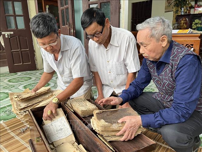 Các thành viên ban quản lý di tích Đền Quốc Tế bên các cuốn sách cổ và sắc phong hiện được lưu giữ tại nhà dân. Ảnh: TTXVN