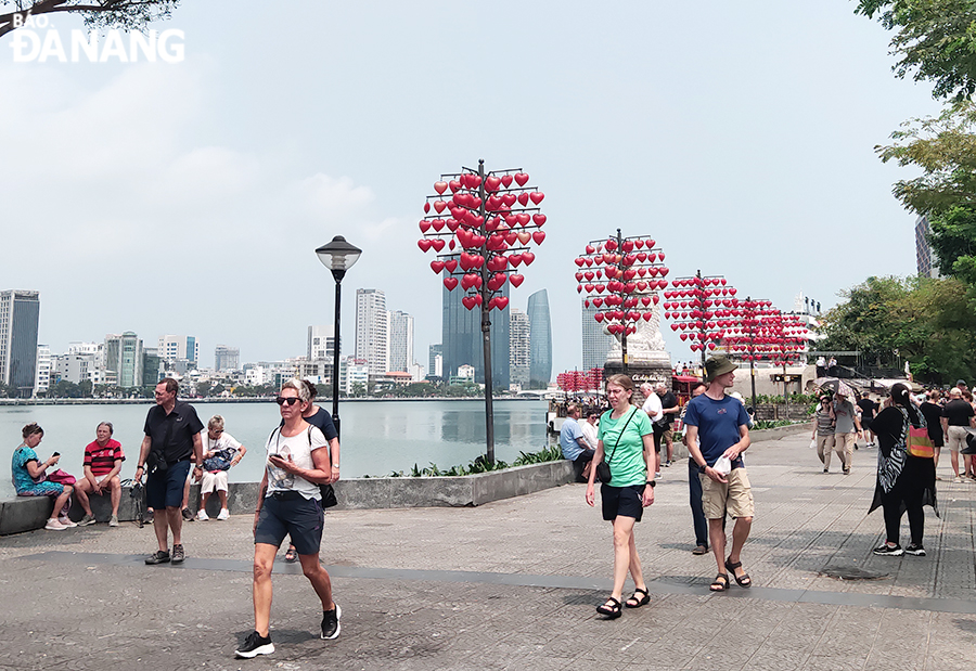  International tourists visit at eastern end of the Dragon Bridge, watching the fish statue ‘squirting water’ on Tran Hung Dao Street.