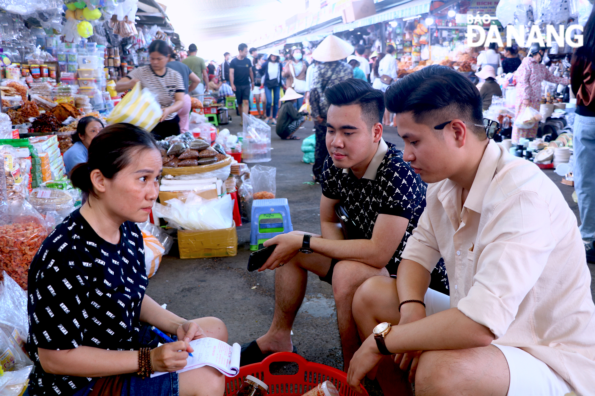 Con Market traders are advising on goods and their prices for 2 tourists from Ha Noi.