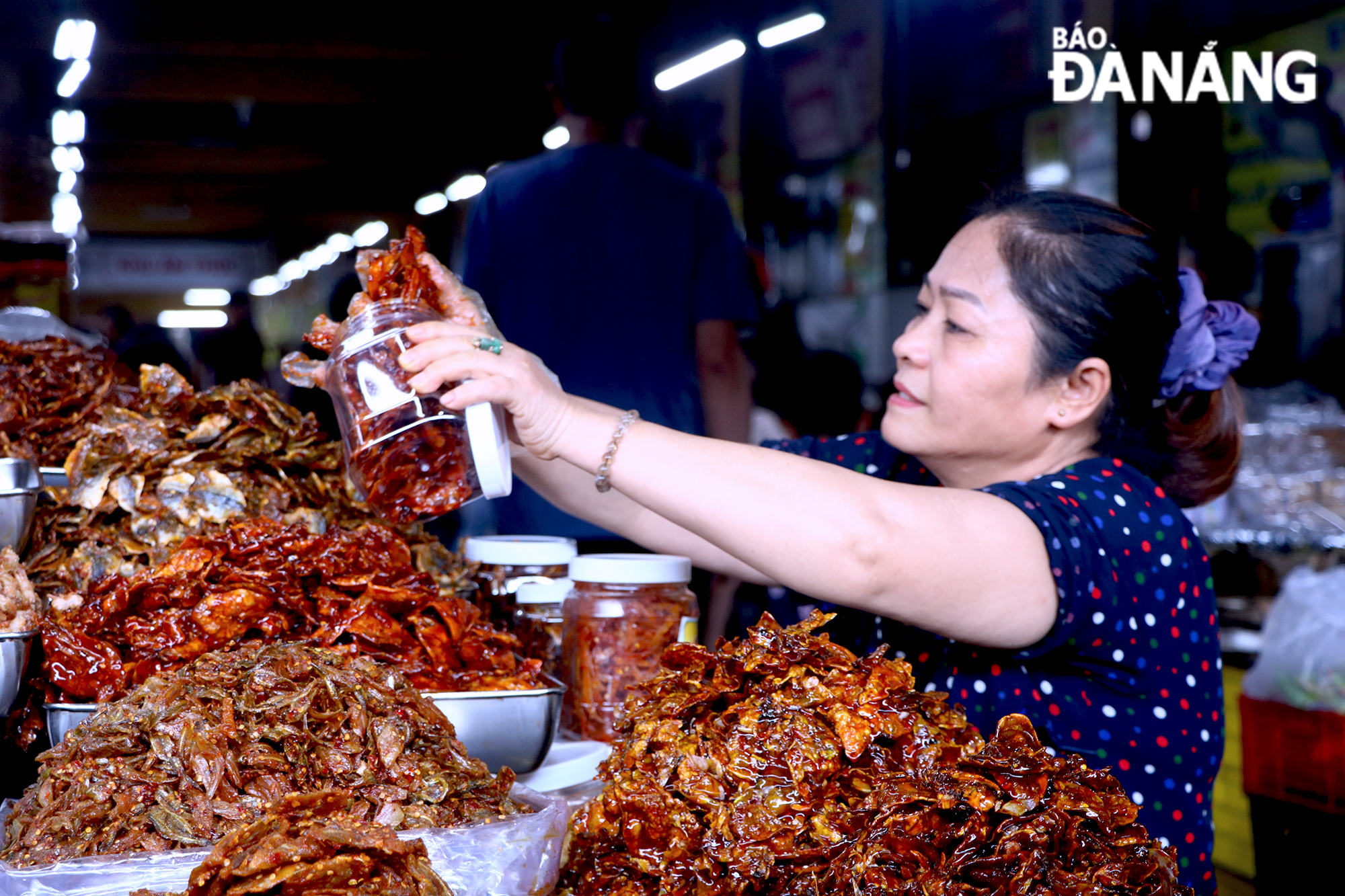   Ms. Truong Thi Ly, the owner of a shop trading in dry goods at Con Market is selling goods to tourists.