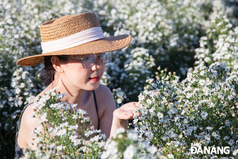 A girl is posing for a photo with white daisies in the afternoon sunlight