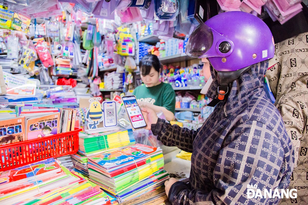 A local woman buys books and school supplies for their children, using non-cash payments.