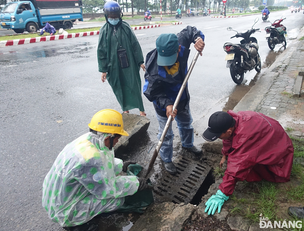 Các công nhân của Công ty Thoát nước và xử lý nước thải Đà Nẵng đội mưa khẩn trương nạo vét cửa thu nước mưa trên đường Nguyễn Tất Thành để chống ngập.