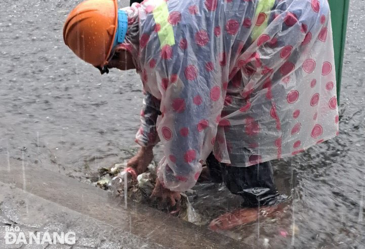 A sanitation workers of the Da Nang Urban Environment Joint Stock Company collect trash stuck at a rainwater intake to ensure drainage