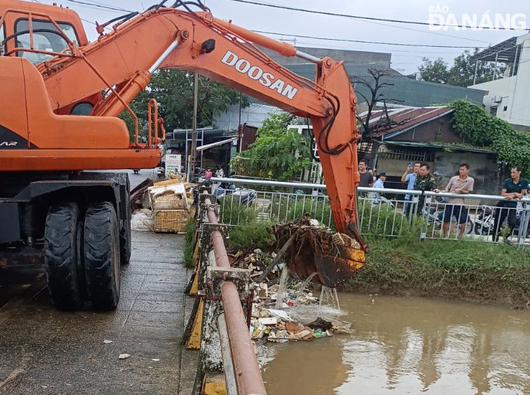 The Da Nang Drainage and Wastewater Treatment Company uses a motorized vehicle to dredge trash stuck at a canal bridge to clear drainage.