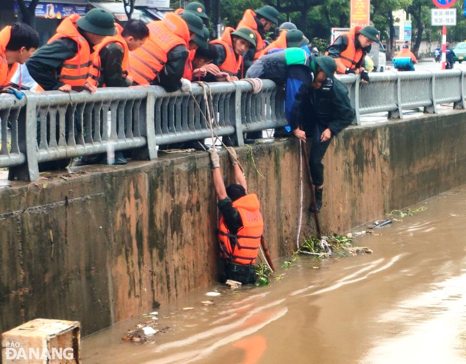 Lực lượng quân đội đu dây vớt bèo, rác mắc kẹt tại cầu qua kênh Đa Cô để khơi thông thoát nước, chống ngập úng tại khu vực đường Mẹ Suốt, Hoàng Văn Thái vào sáng 17-10. Ảnh: PV