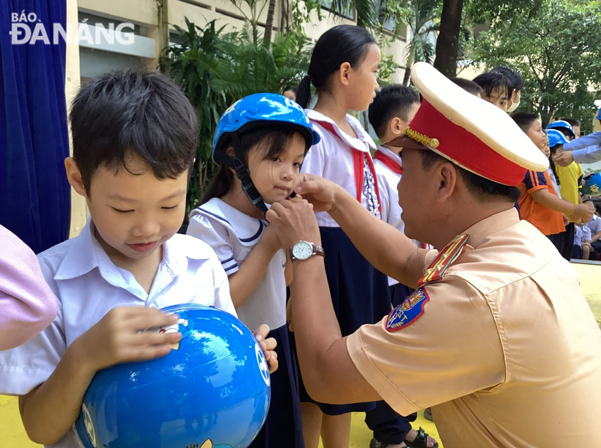 Leader of the Traffic Police Department helps pupil put on helmets. Photo: THANH LAN