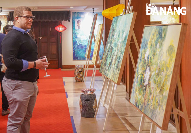 Vị khán giả nước ngoài tỏ ra thích thú với những bức tranh sơn dầu vẽ hoa sen của họa sĩ Thành Nguyễn. Ảnh: T.Y