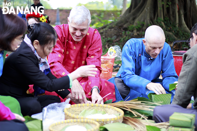 Foreign tourists experience wrapping traditional 'banh chung' at the event.