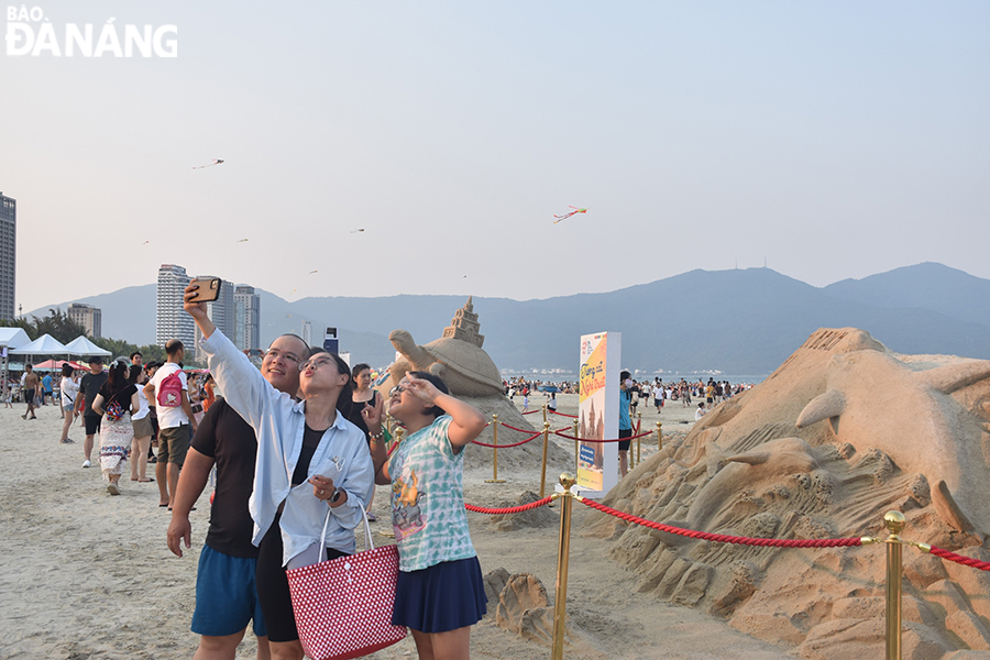 Visitors enjoy taking commemorative photos at the sand sculpture exhibition. Photo: THU HA