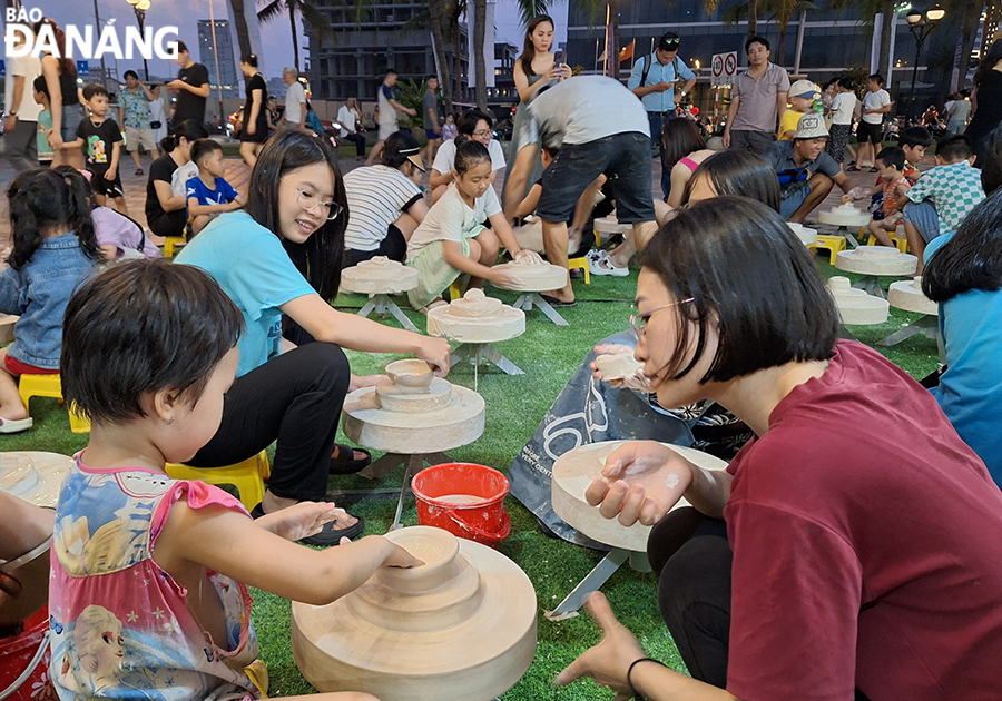 A large number of people and tourists, especially children, showing their excitement at experiencing the stages of making pottery products. Photo: THU HA