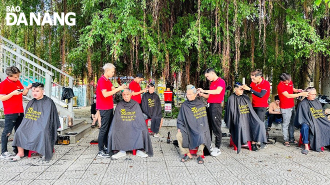 Barbers from Vuong Barber Shop are cutting hair for free for people on the sidewalk of a section of Nguyen Tri Phuong Street near the March 29 Park